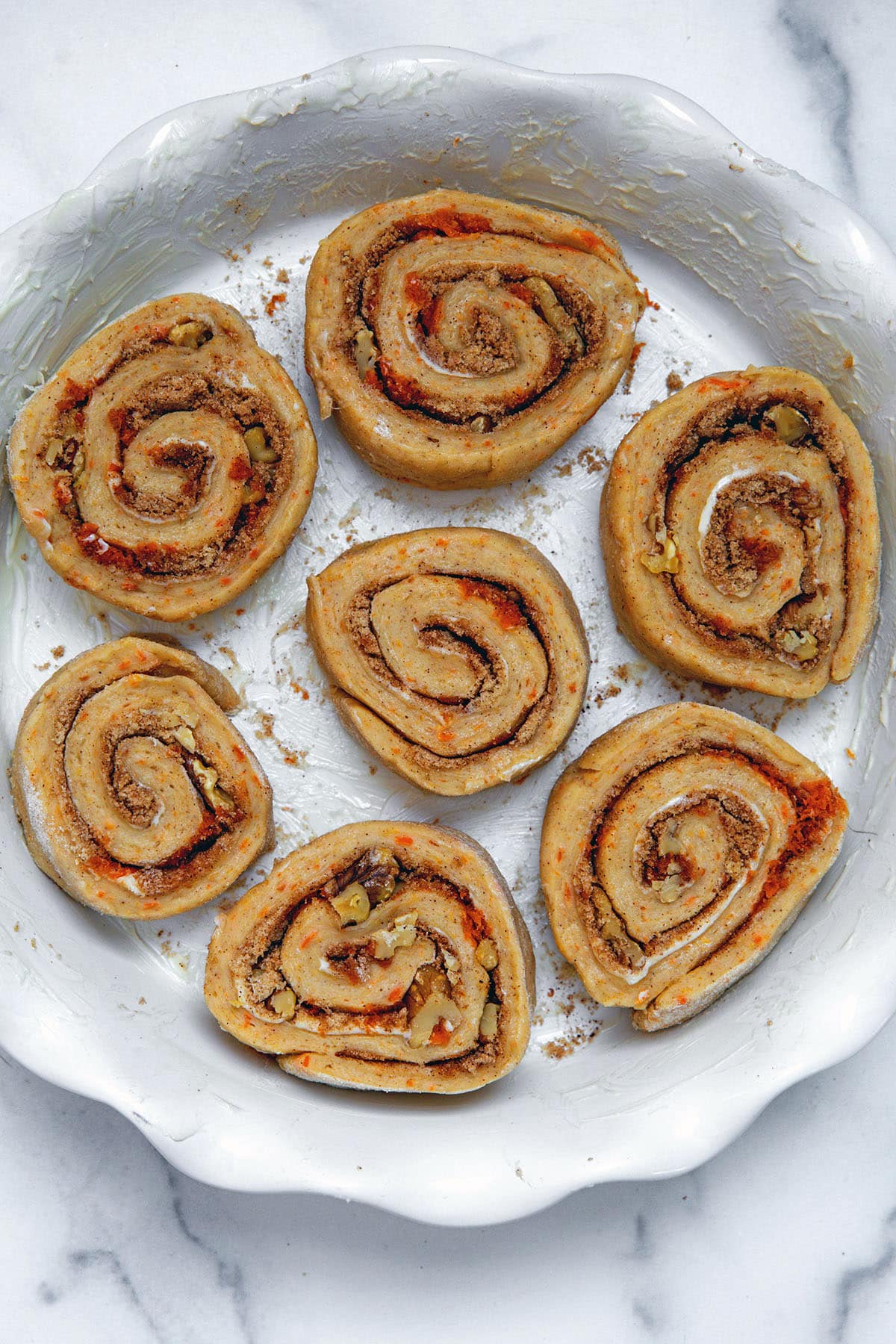 Unbaked carrot cake cinnamon rolls in a pie dish.