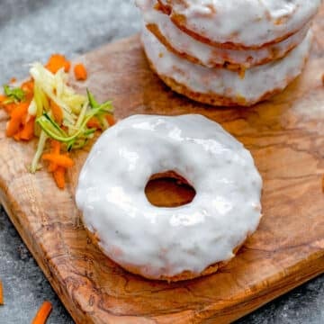 Closeup view of a frosted carrot zucchini donut on a wooden board with grated carrots and zucchini.