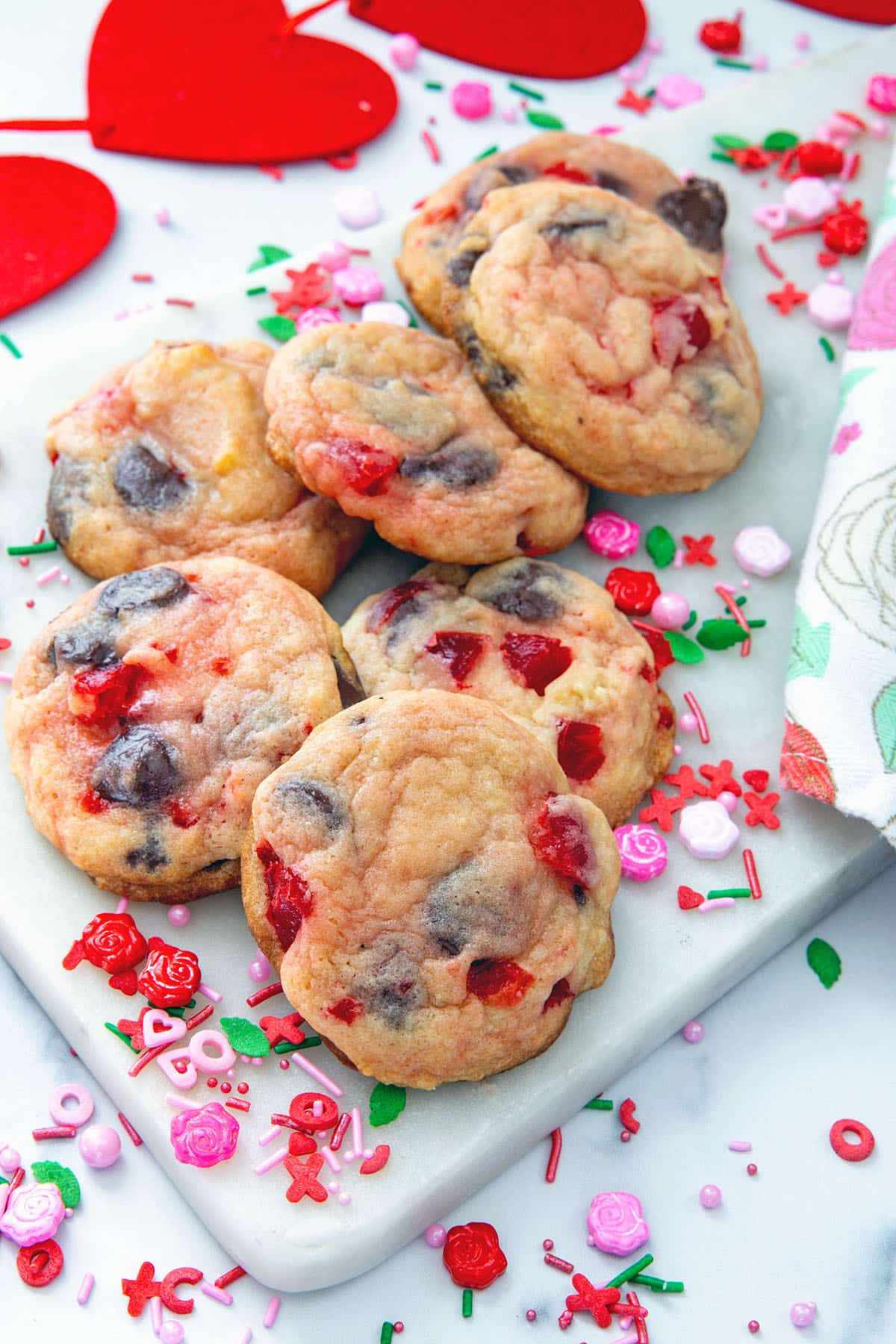 Cherry chocolate chip cookies on a marble platter with Valentine's Day sprinkles all around.