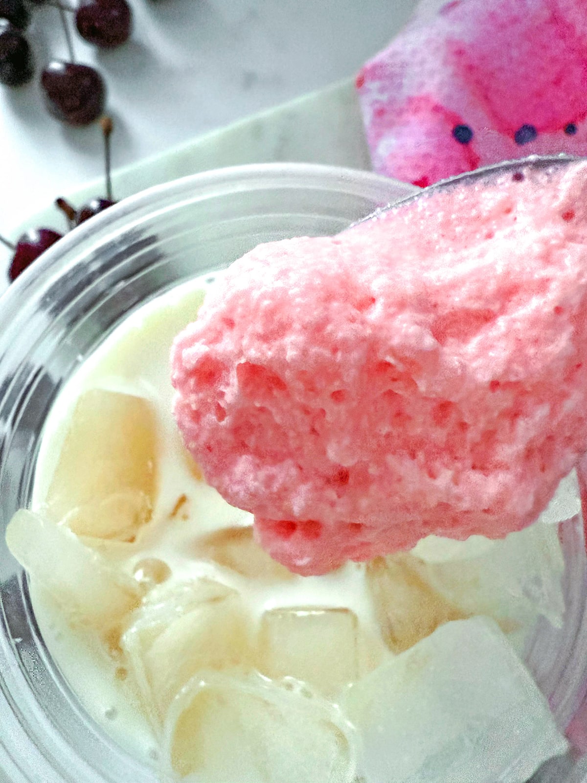 Cherry cold foam being spooned onto chai and milk mixture with ice.