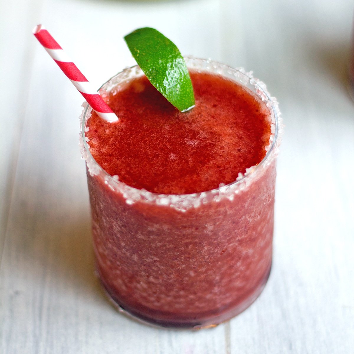 Closeup view of a frozen cherry lime margarita with lime wedge garnish.