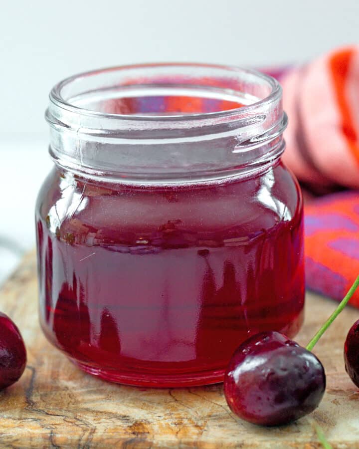 Close-up view of a small jar of cherry syrup with fresh cherries around.