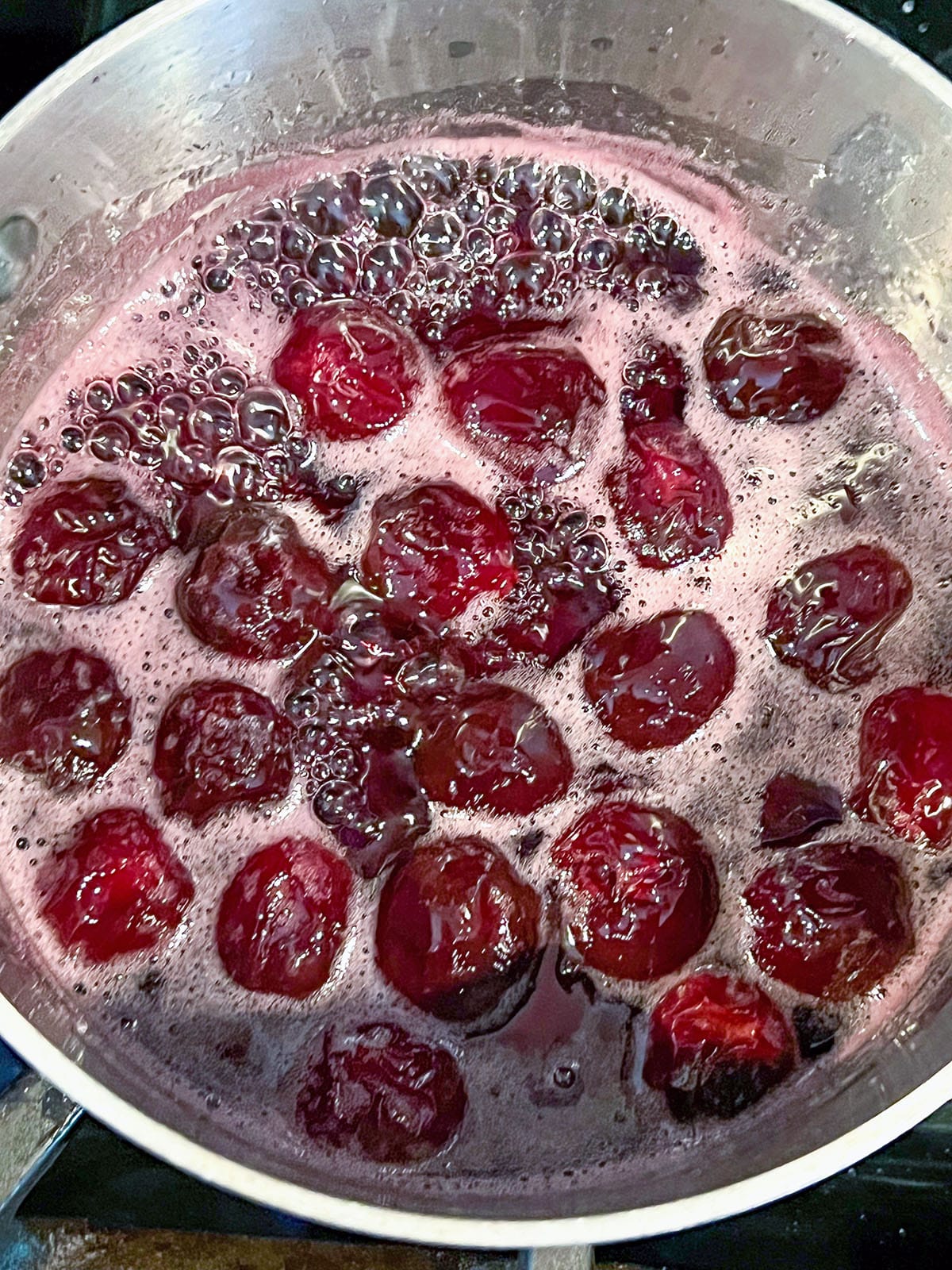 Cherries simmered and breaking down in water and sugar in saucepan.