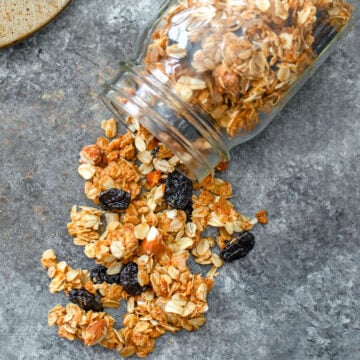 Overhead view of cherry vanilla granola spilling out of a mason jar onto a grey surface.