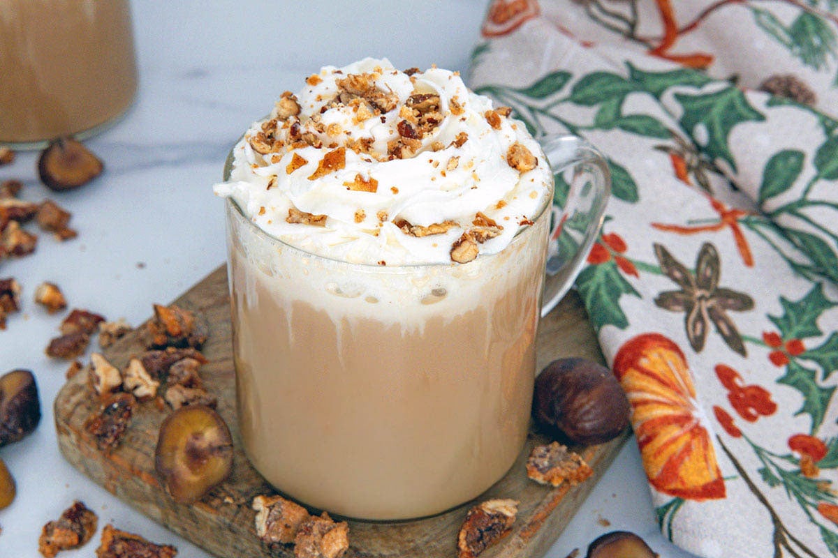Overhead view of a Chestnut Praline Latte with whipped cream and chestnut praline crumble topping and nut pieces all around.