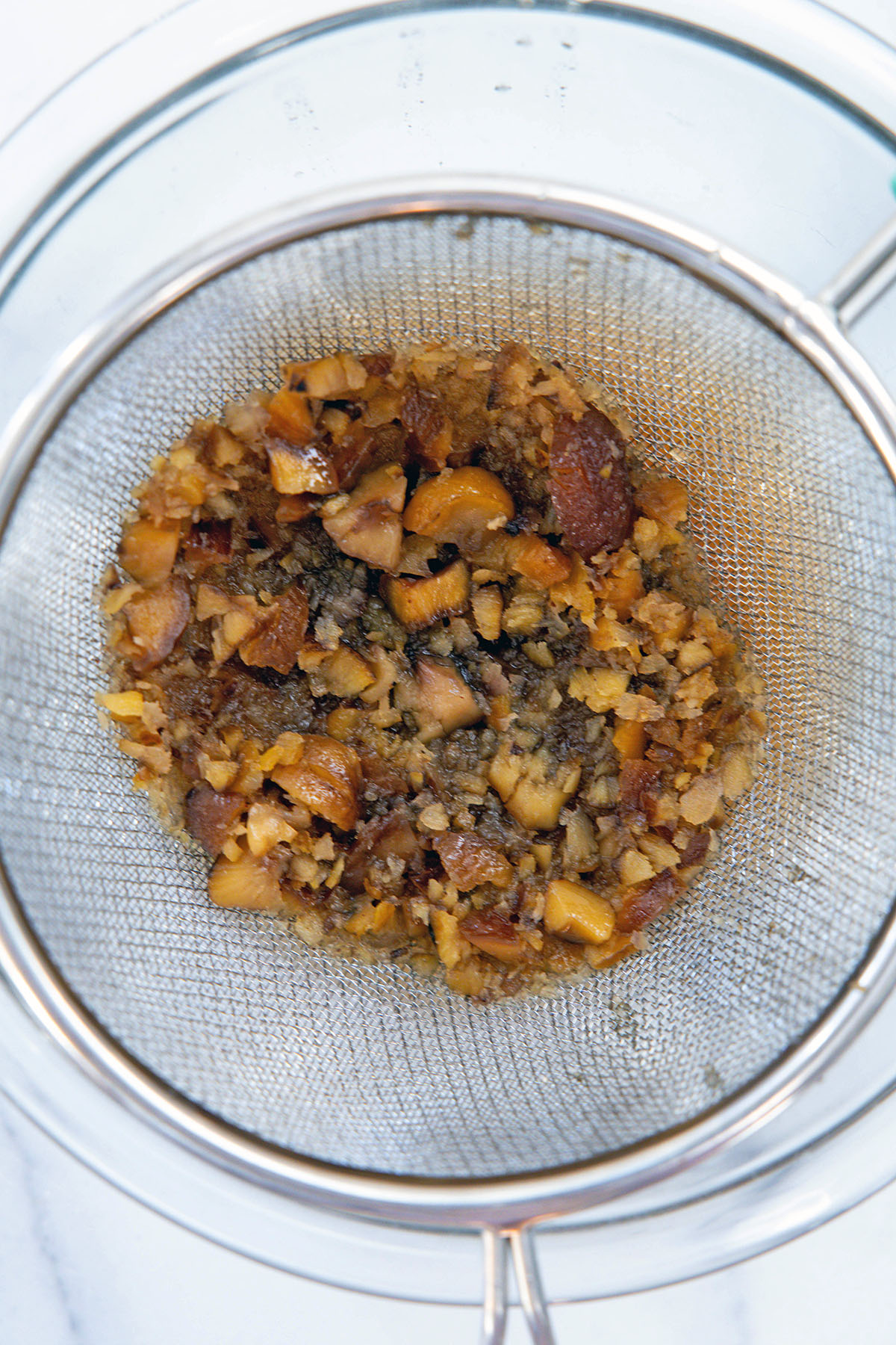 Overhead view of chestnut pieces being strained out of syrup into a bowl.