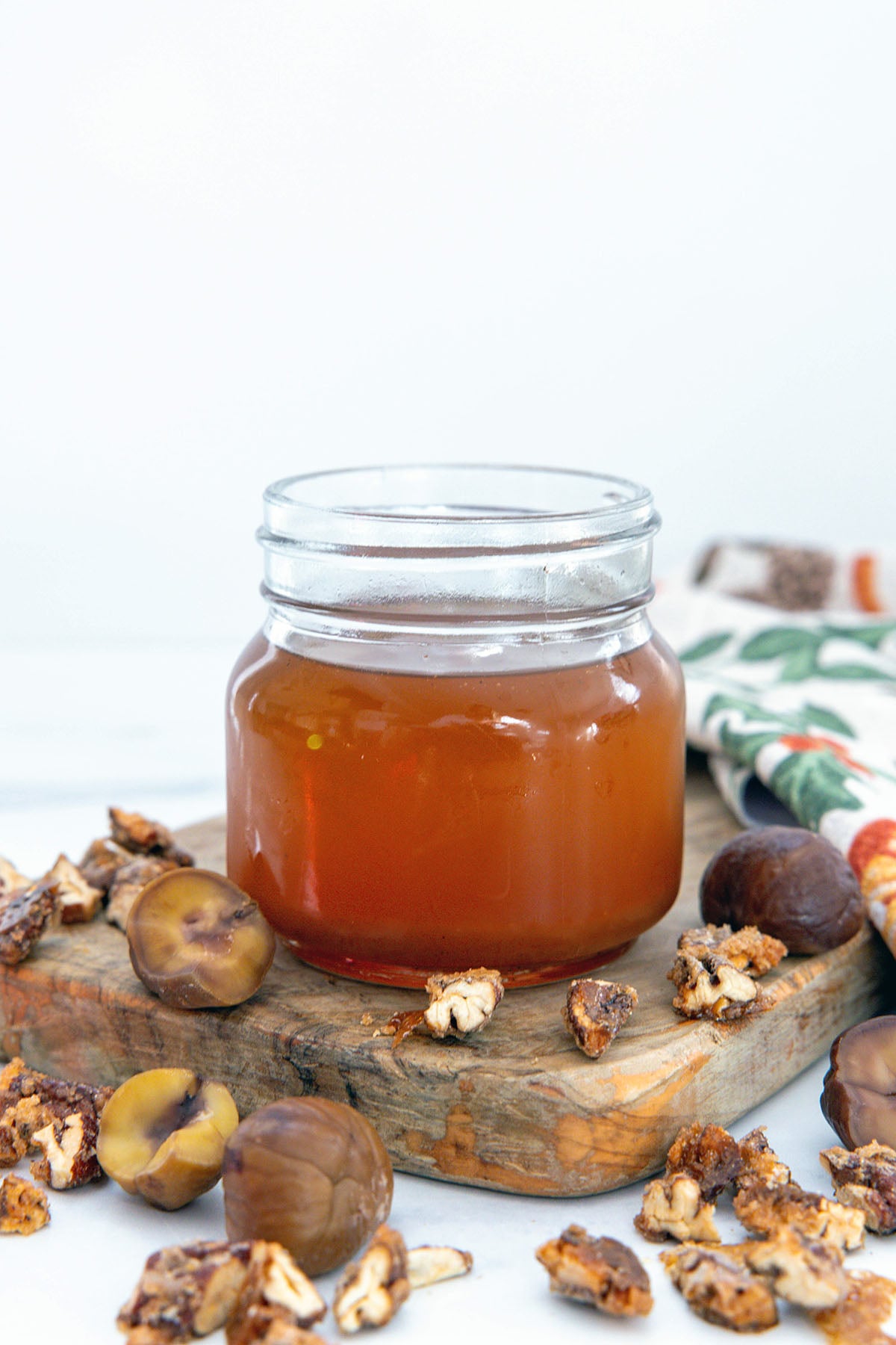 Chestnut praline syrup in a small jar with chestnut and praline pieces all around.