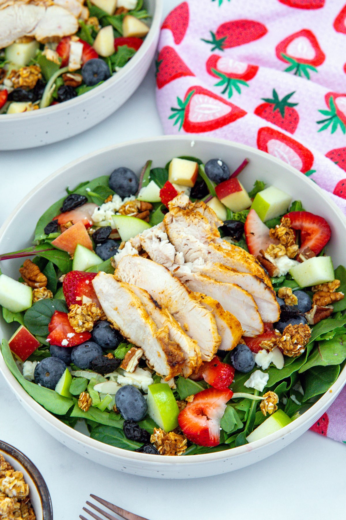Closeup overhead view of a salad with grilled chicken, blueberries, apples, strawberries, granola, blue cheese, and more.