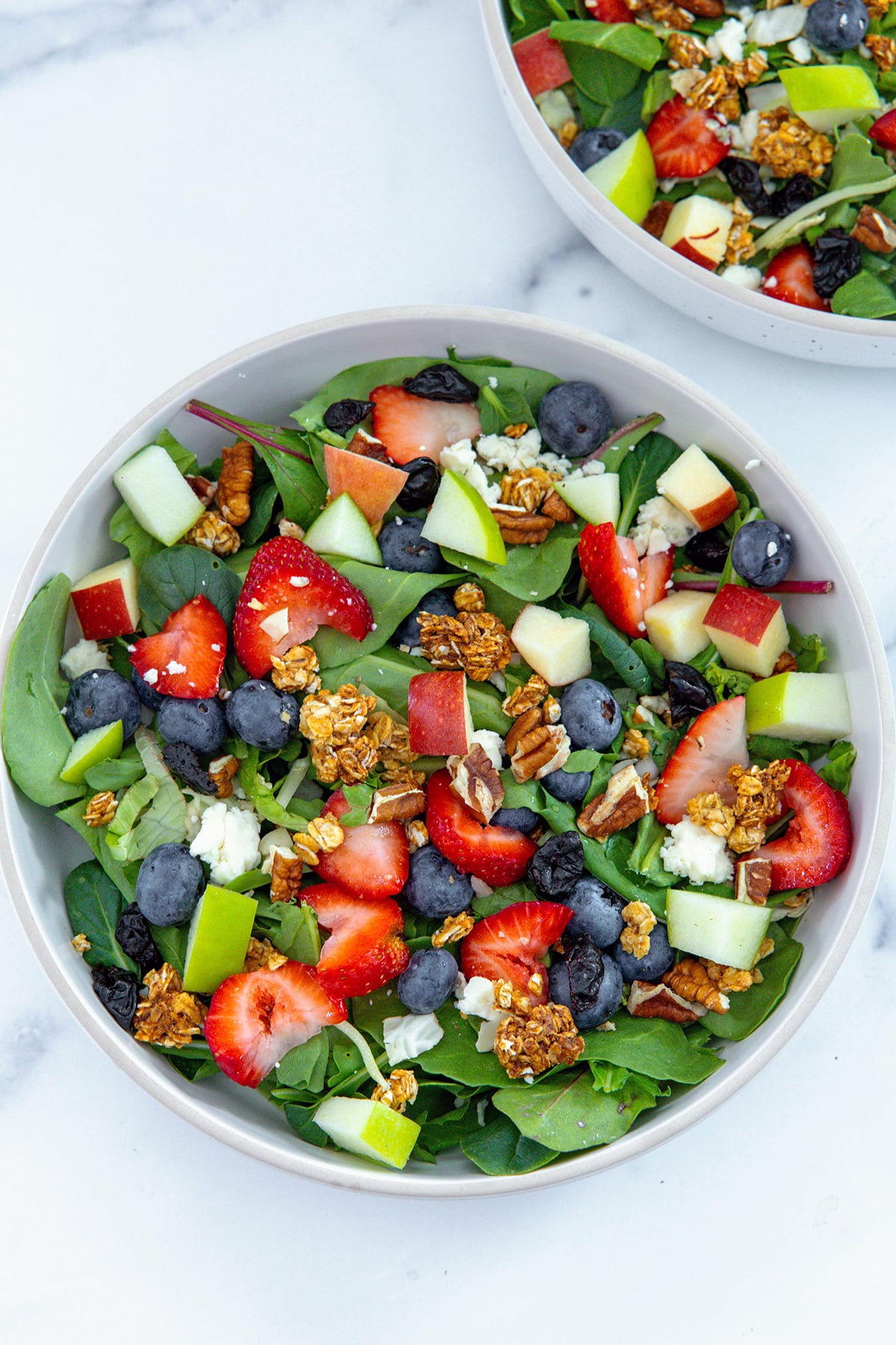 Salad ingredients including lettuce, fruit, and granola tossed in a bowl.