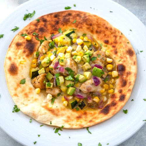 Overhead closeup of a chicken and vegetable tostada with corn, zucchini, salsa verde, and more.
