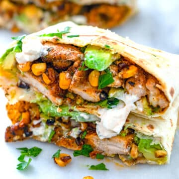 Closeup view of a chicken avocado and corn burrito with feta cheese.