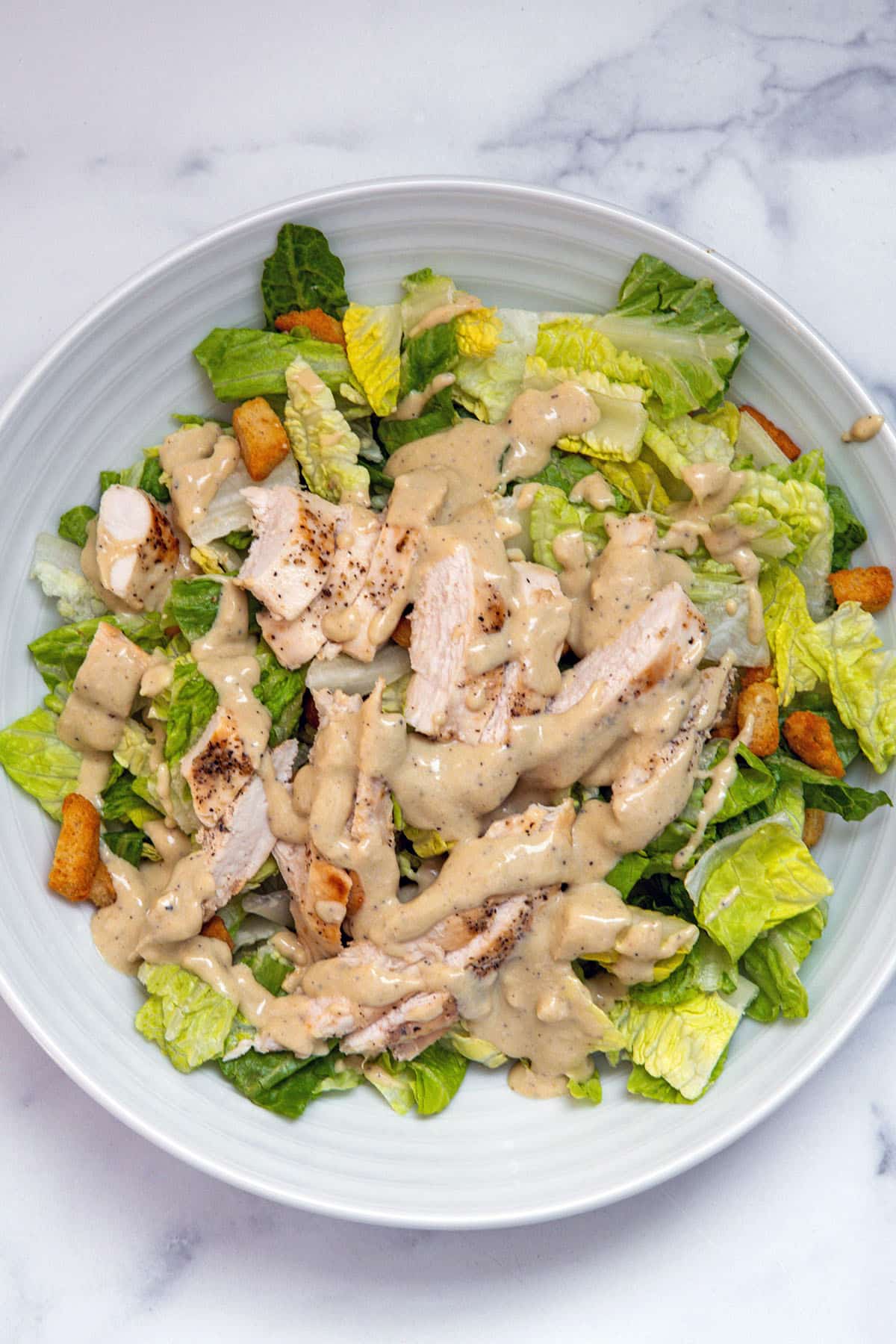 Overhead view of caesar salad with croutons and sliced chicken on top.