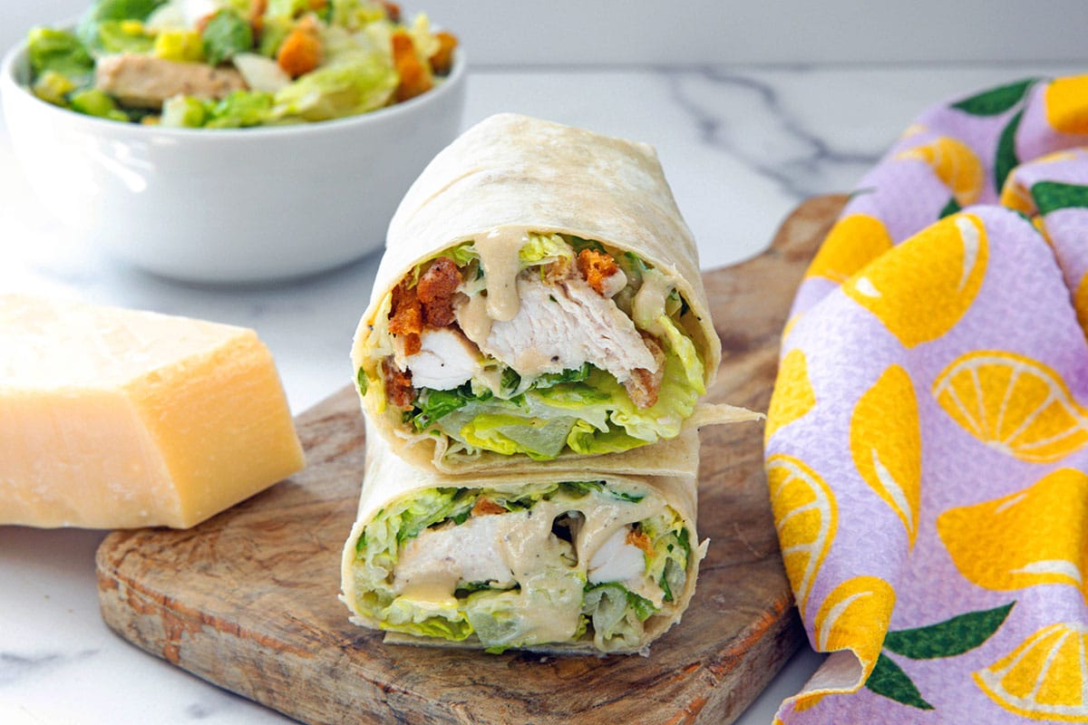 Landscape head on view of chicken caesar wraps with block of parmesan cheese and bowl of salad.
