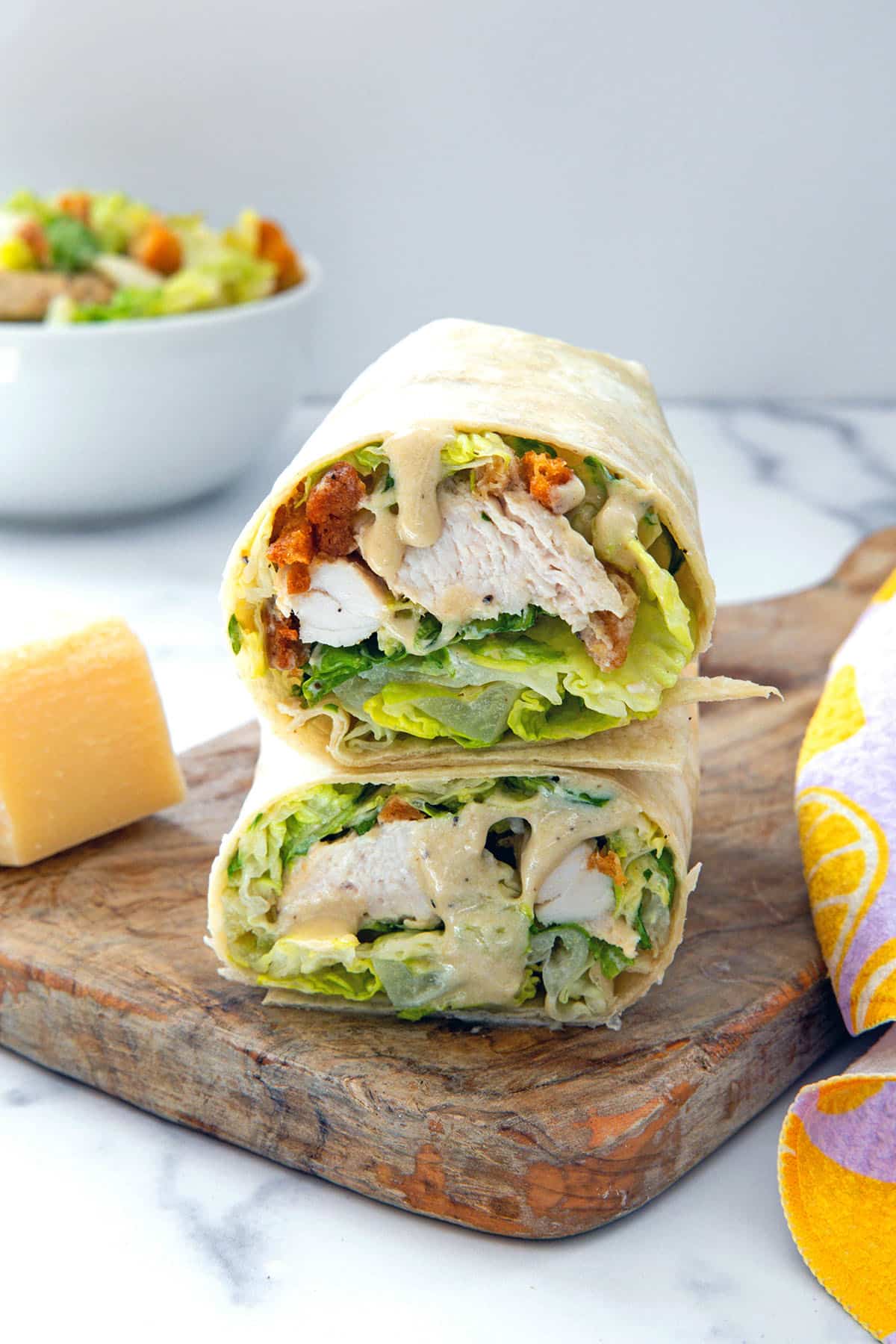 Head-on view of chicken caesar wraps stacked on each other on wooden board.
