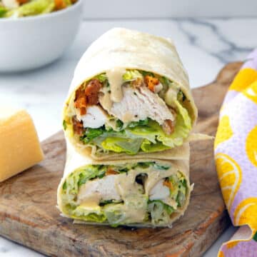 Closeup view of a grilled chicken caesar wrap cut in half and stacked in a wooden board.