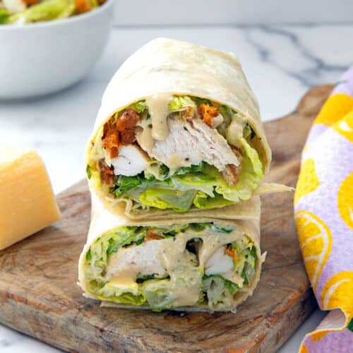 Closeup view of a grilled chicken caesar wrap cut in half and stacked in a wooden board.