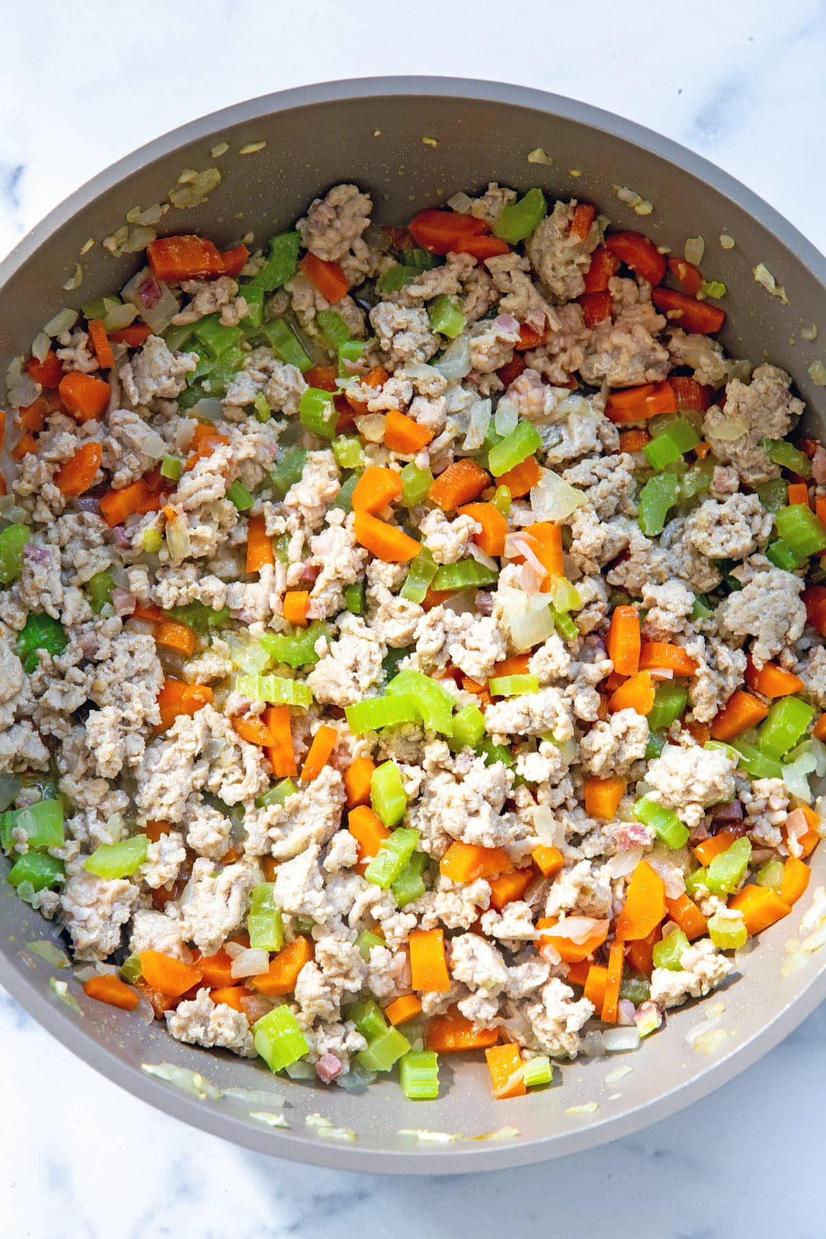 Ground chicken in skillet with diced carrots, celery, and onion.