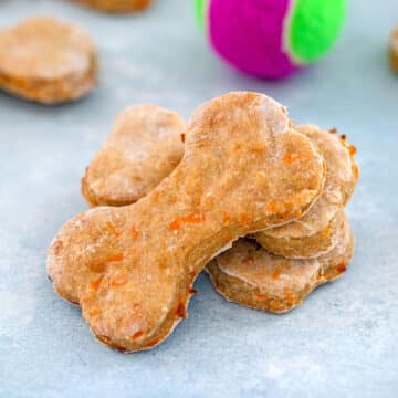 Closeup view of chicken dog treats shaped like dog bones with tennis ball in background.