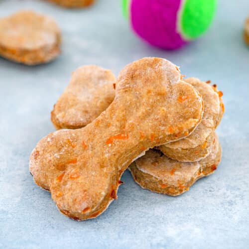 Closeup view of chicken dog treats shaped like dog bones with tennis ball in background.