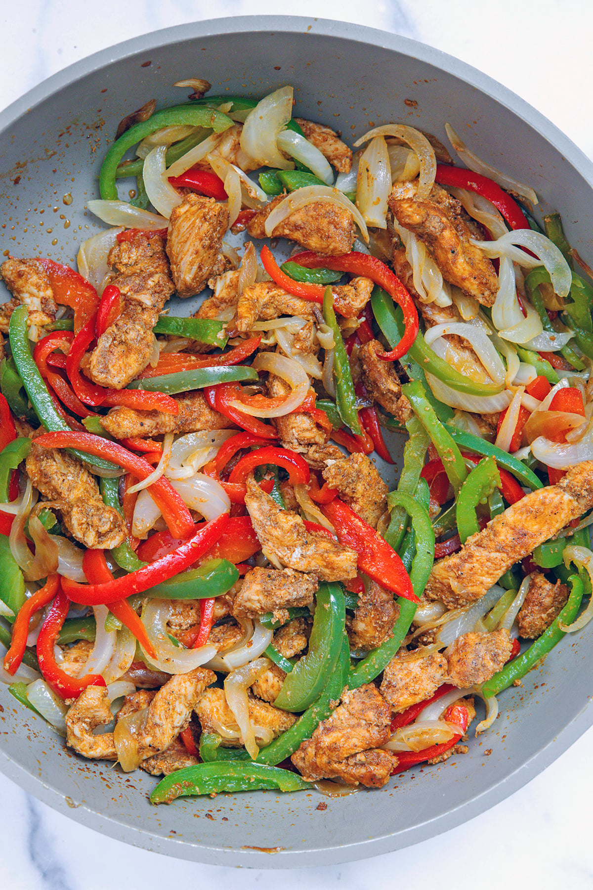 Chicken, peppers, and onions cooking in a skillet.