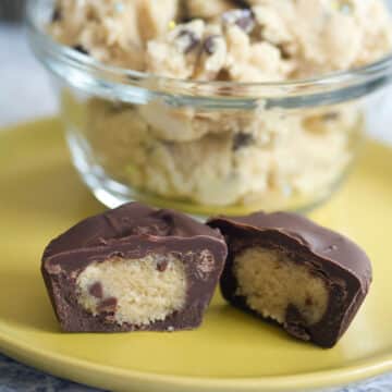 Closeup view of chocolate cookie dough cups cut in half to show filling with bowl of cookie dough in background.