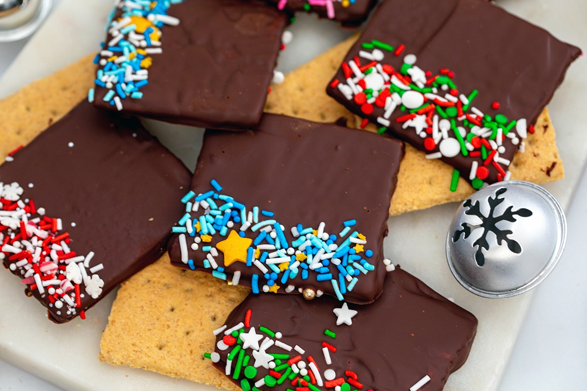 Landscape overhead view of chocolate covered graham crackers with sprinkles and a Christmas bell.