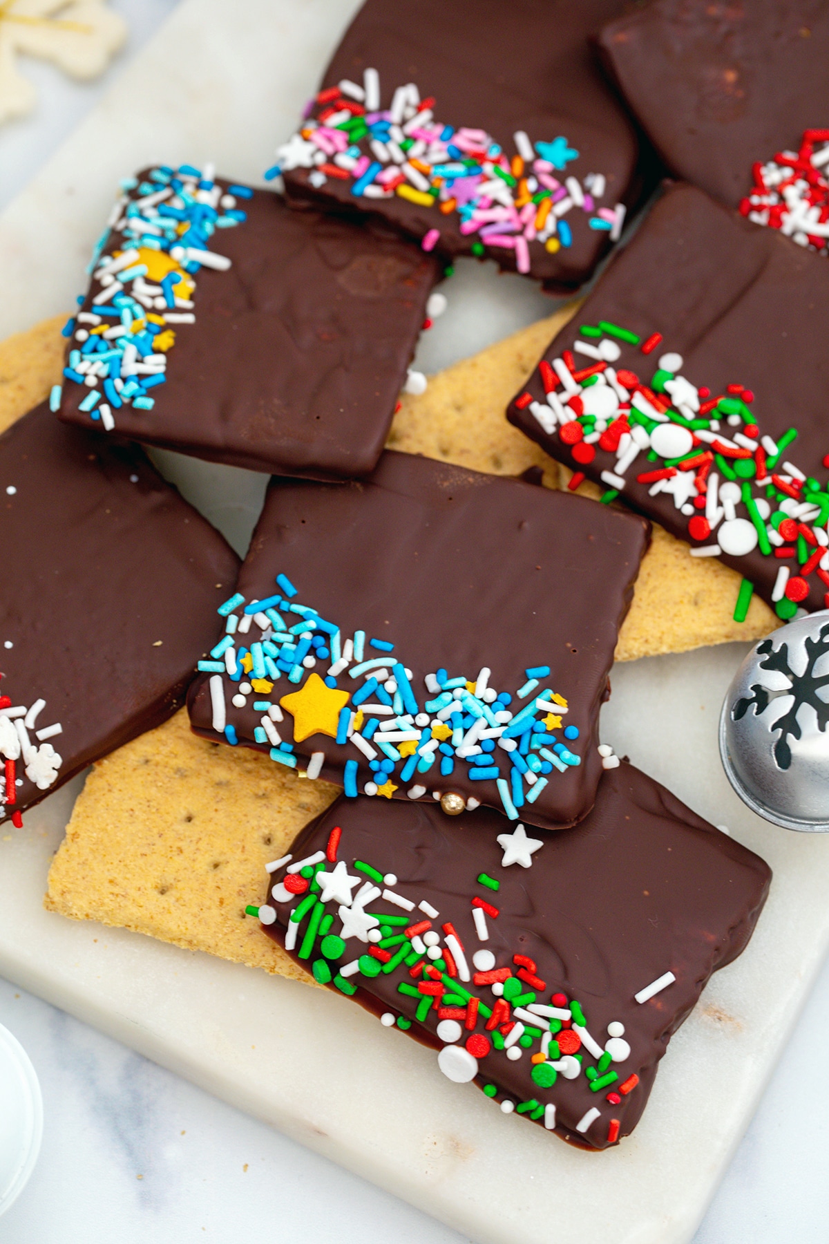 Chocolate covered graham crackers with sprinkles stacked on marble platter.