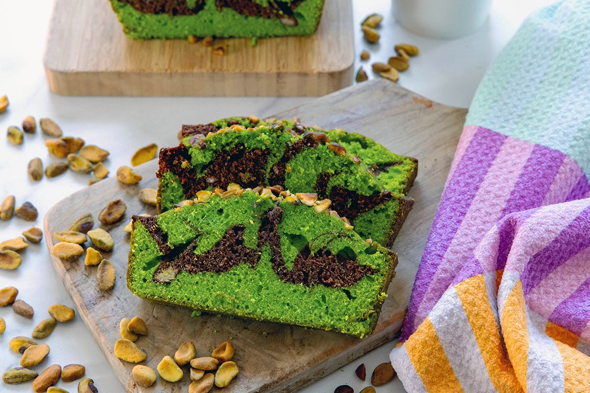 Head-on landscape view of two slices of swirled chocolate pistachio loaf with pistachios all around.