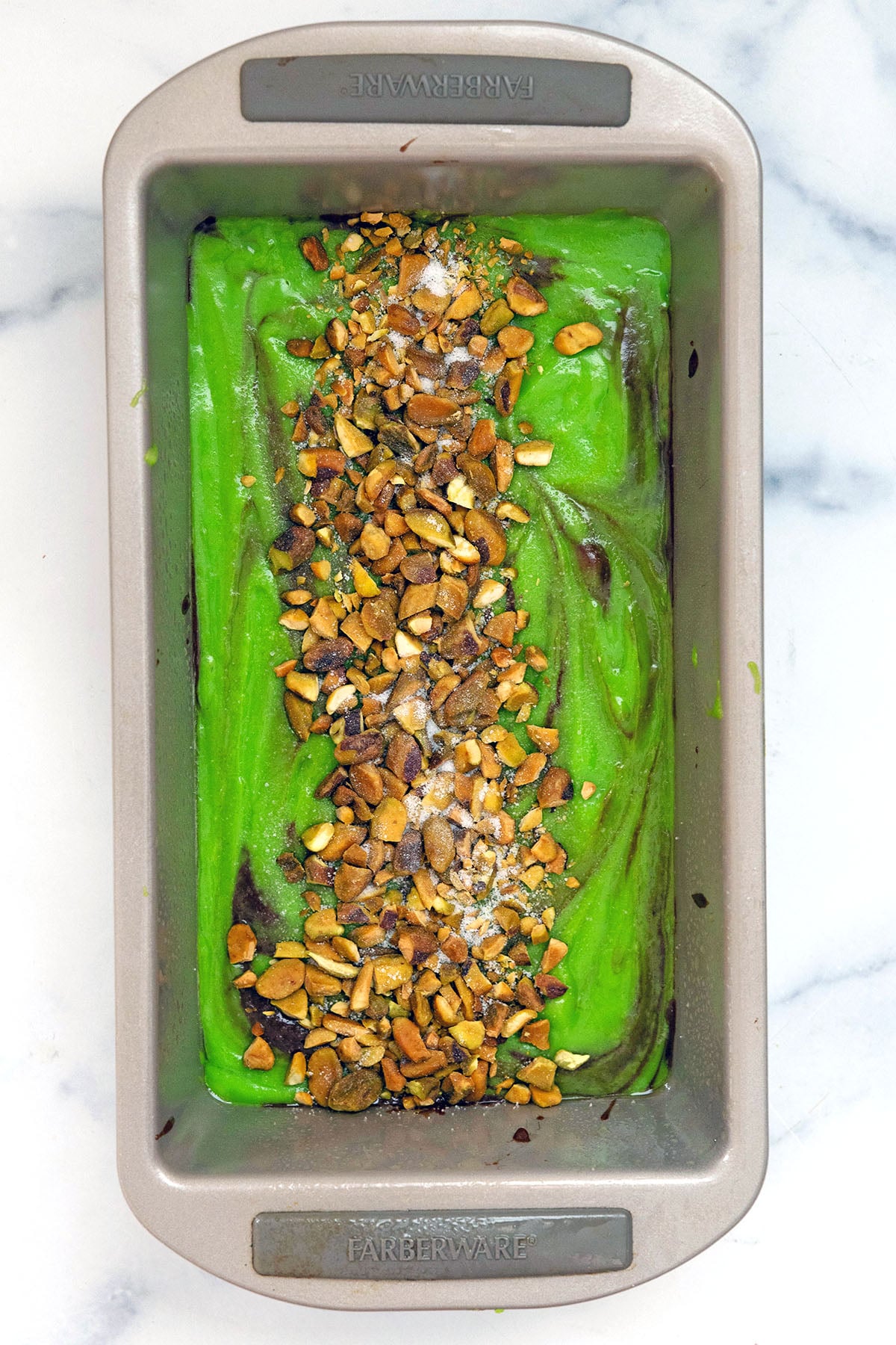 Green batter in loaf pan topped with pistachios down the middle.