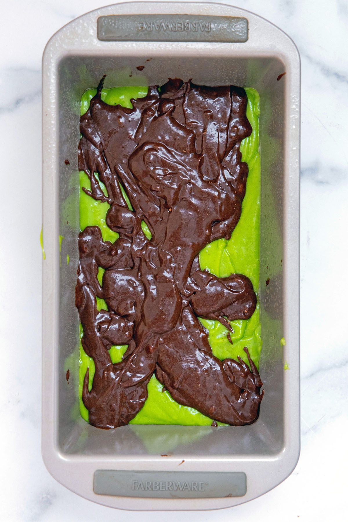Green pistachio batter in loaf pan with chocolate batter in ribbons on top.