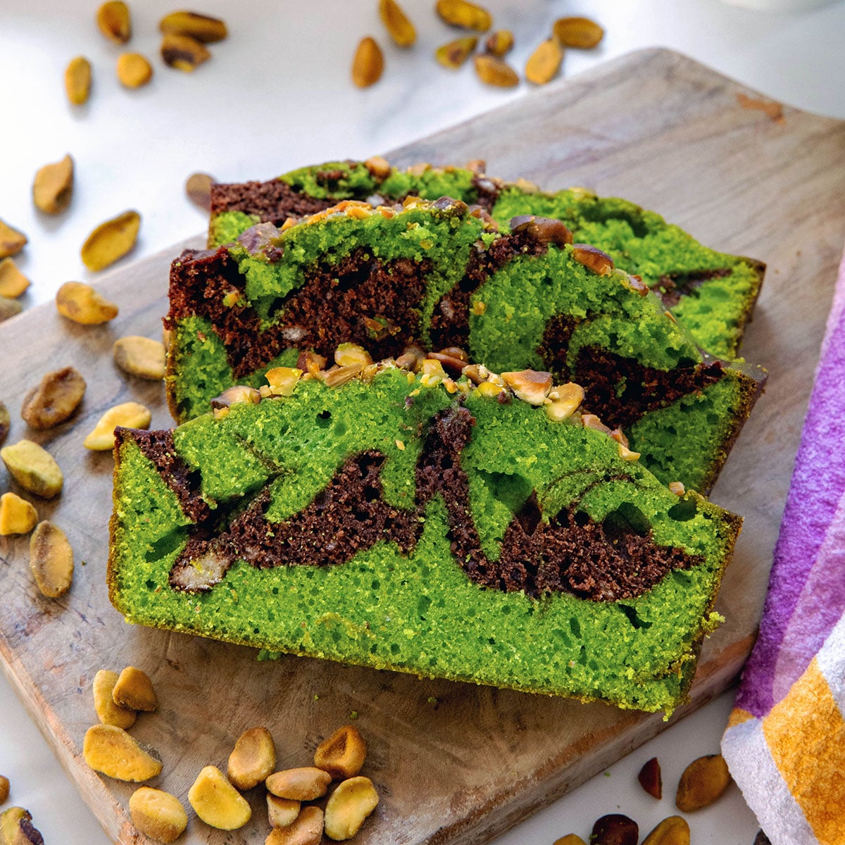 Closeup view of two slices of chocolate pistachio loaf on a wooden board.