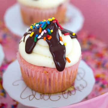 Closeup view of a strawberry cupcake with vanilla frosting and chocolate sauce with sprinkles.