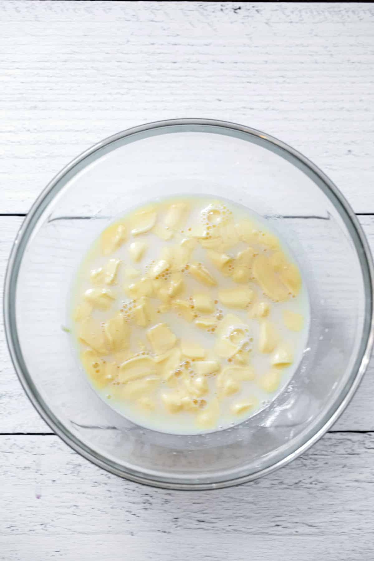 Chopped white chocolate with milk mixture poured over it in small bowl.