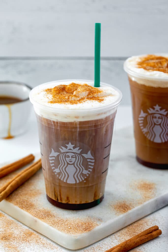 Overhead view of a cinnamon caramel cream cold brew topped with cold foam, cinnamon sugar, and a green straw with cinnamon sticks and cinnamon sugar all around.