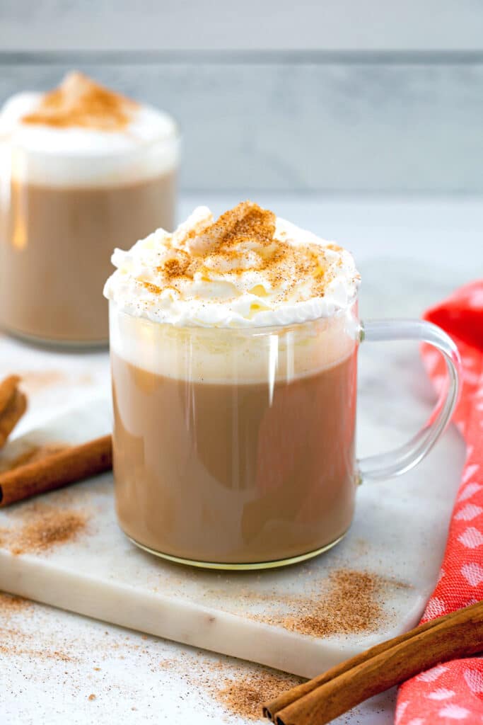 Head-on view of a cinnamon dolce latte with whipped cream and ground cinnamon with cinnamon sticks on the side.