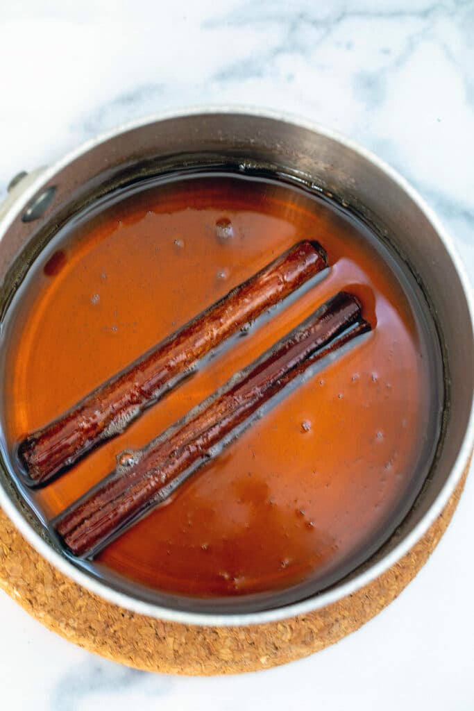Cinnamon sticks simmering in syrup in saucepan.