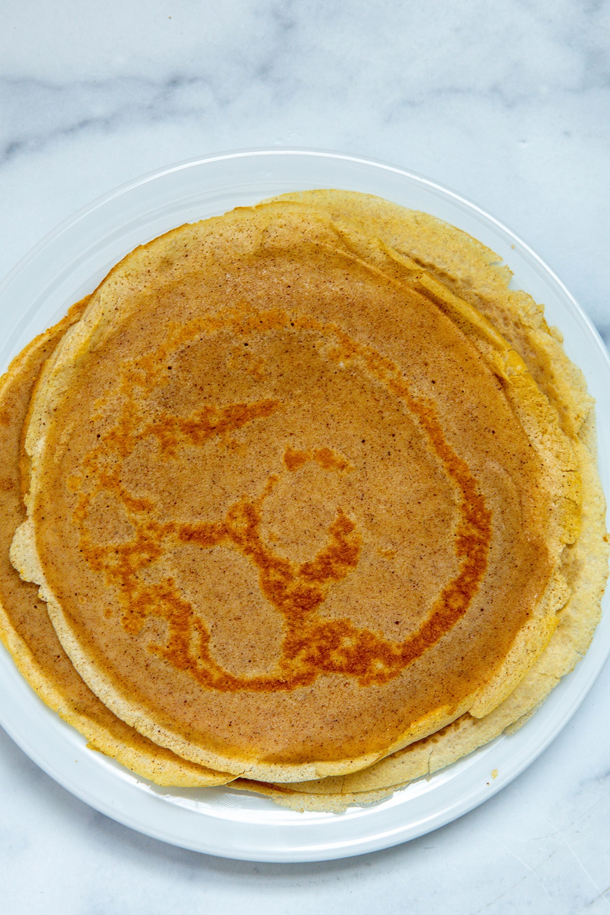 Overhead view of cinnamon crepes stacked on a plate.