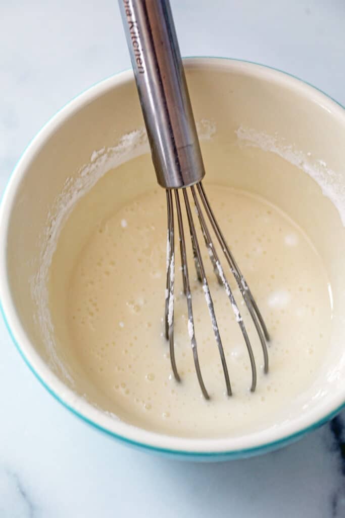 Vanilla icing in bowl with whisk.