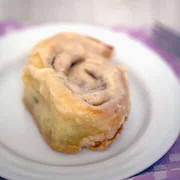 Closeup view of a cinnamon roll on a white plate.