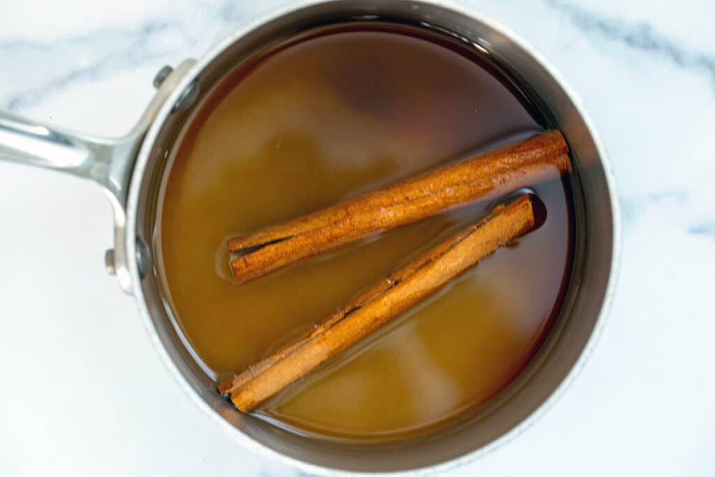 Cinnamon sticks in a saucepan with water and granulated sugar.
