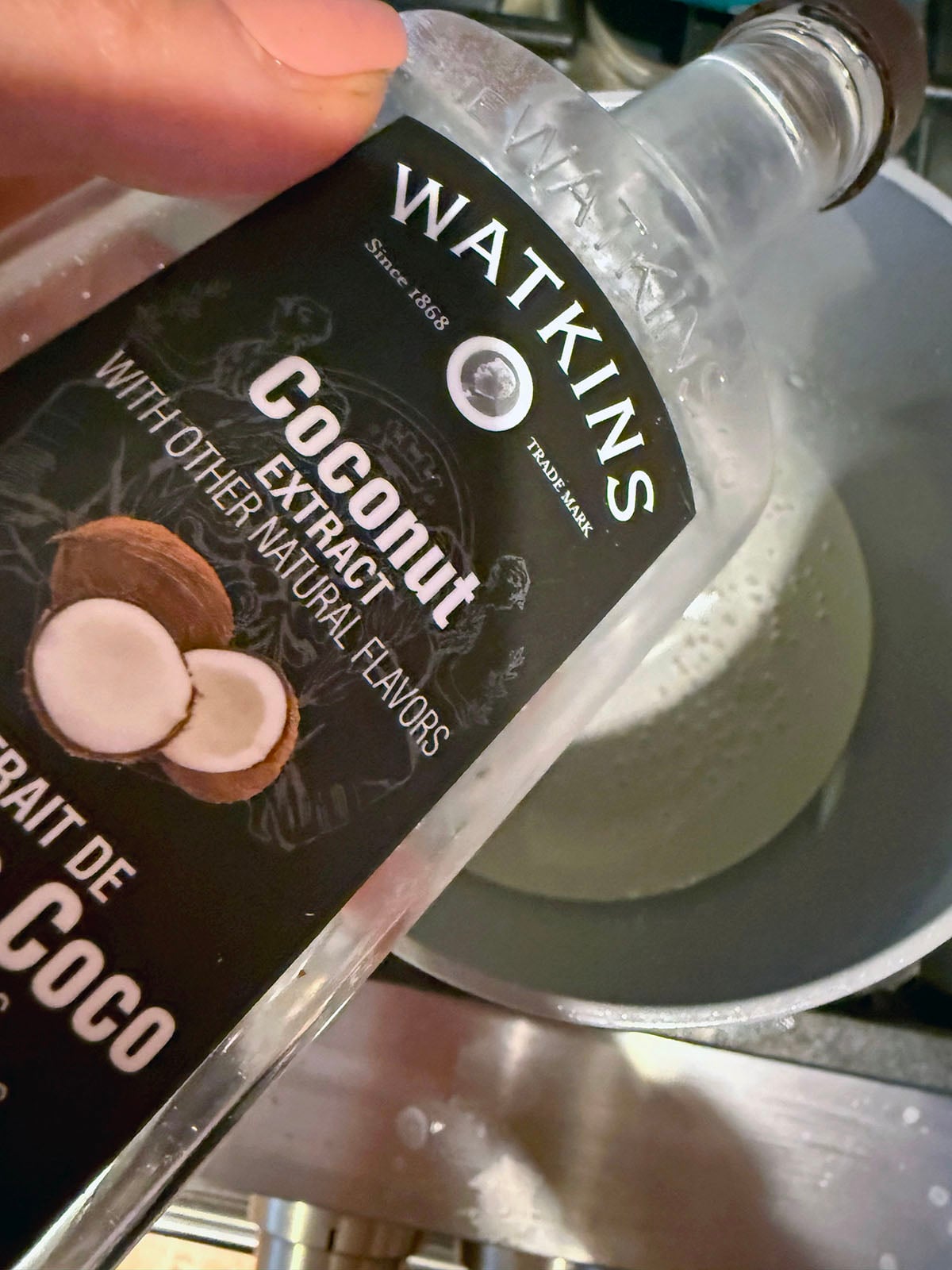 Coconut extract being poured into syrup in saucepan.