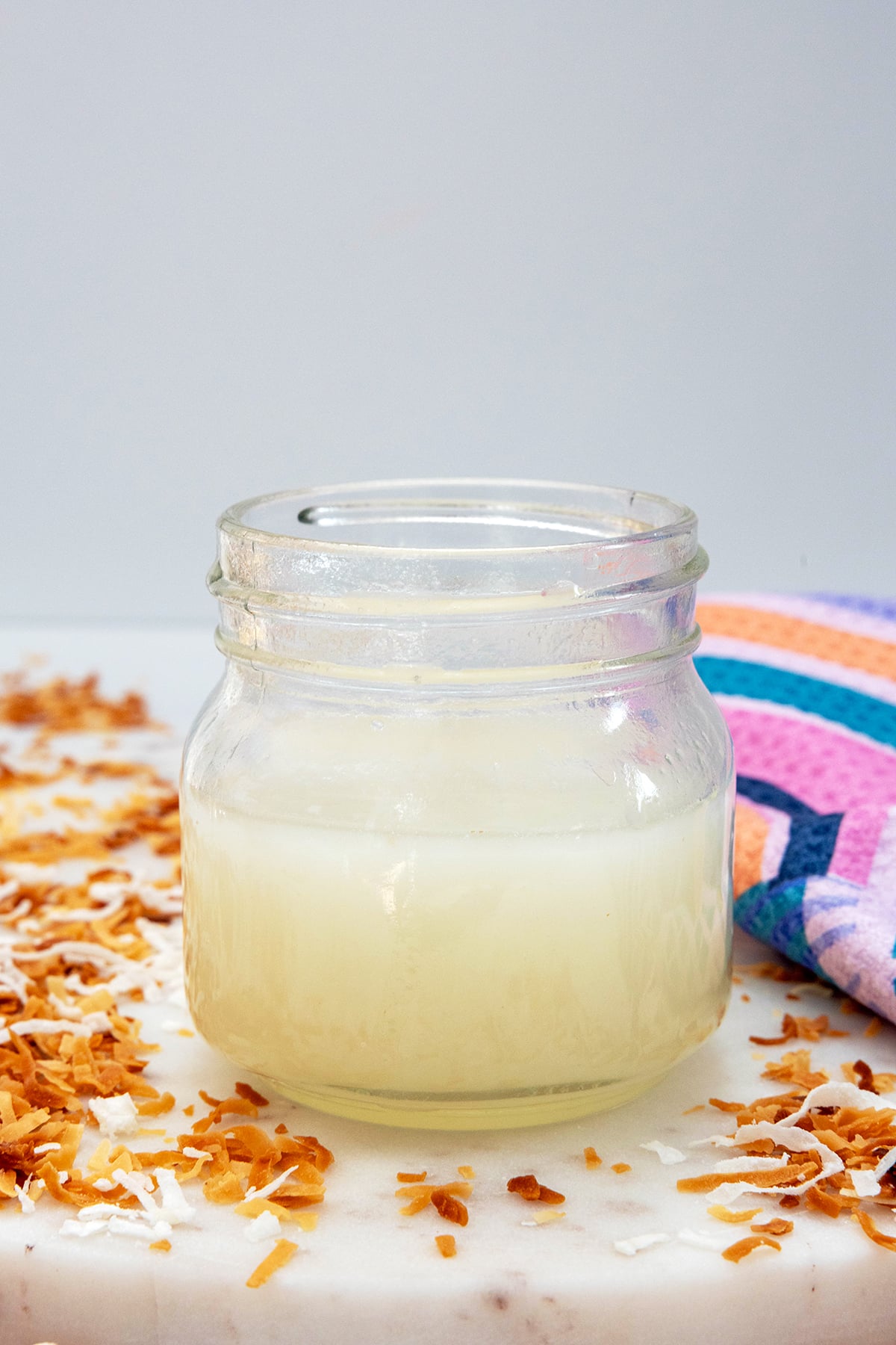 Head-on view of a small jar of coconut syrup with coconut all around.
