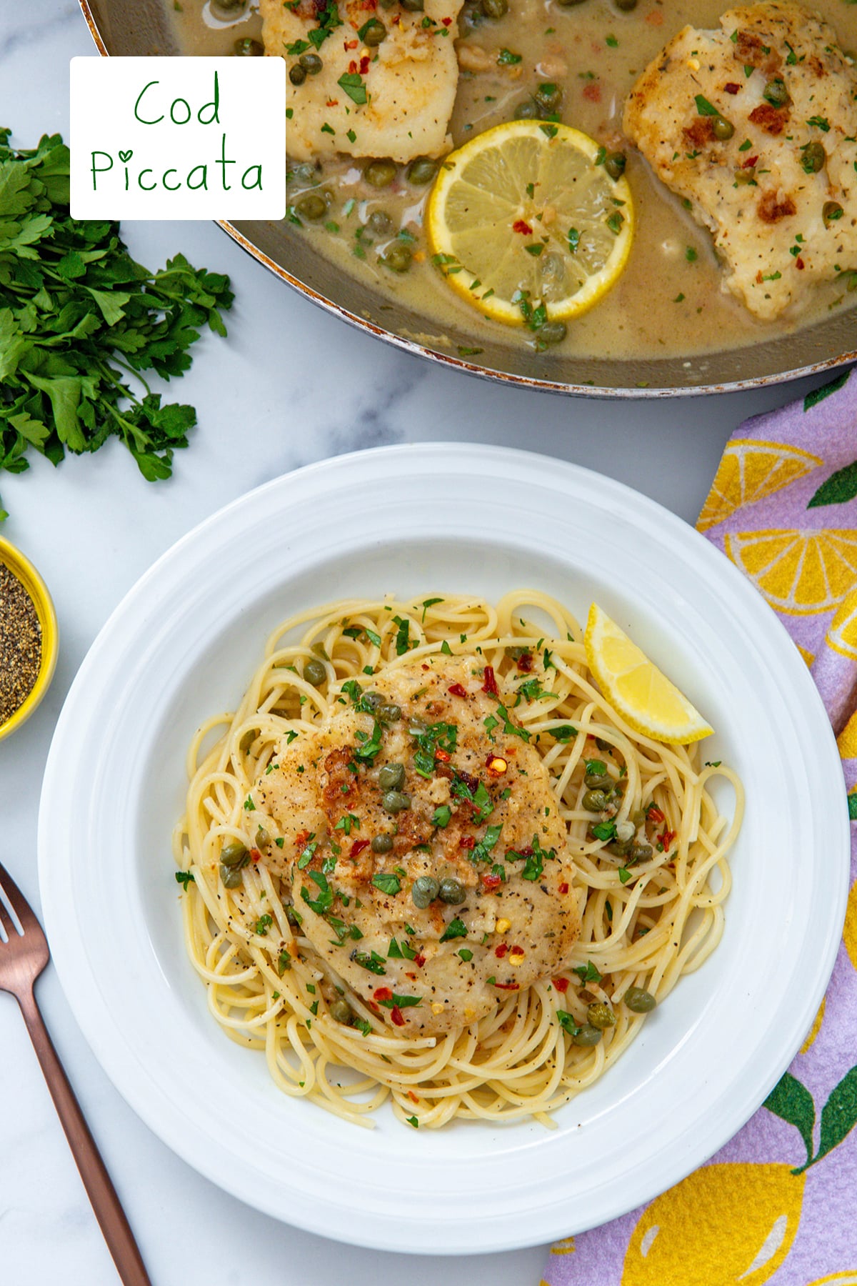 Overhead view of cod piccata served over linguine with skillet of lemon cod in background and recipe title at top.