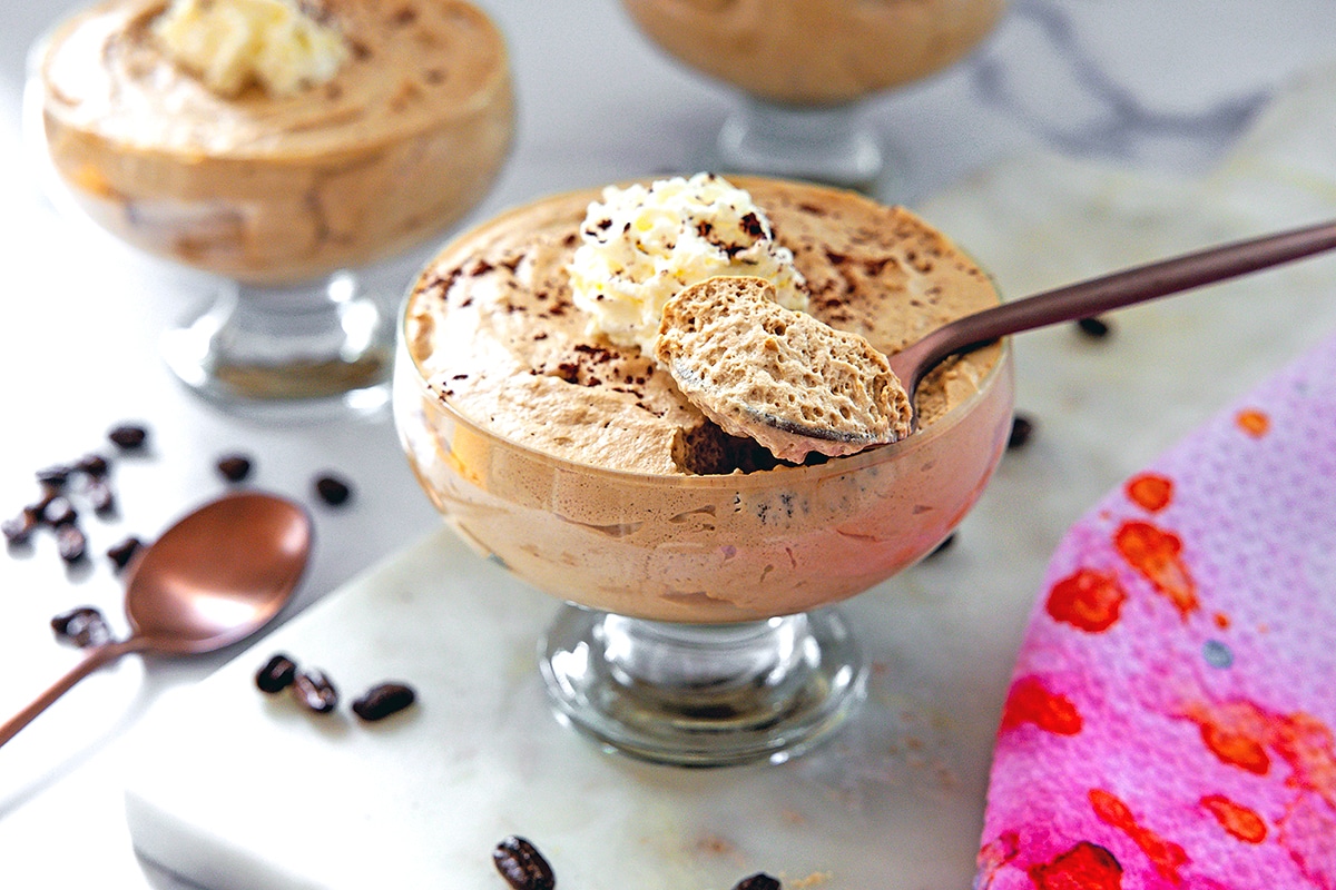Landscape head-on view of a glass ramekin of coffee mousse with spoon taking a scoop out.