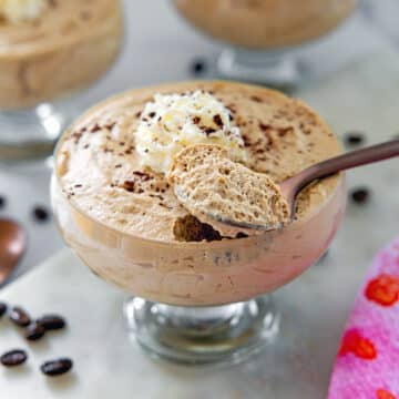 Closeup view of a glass ramekin of coffee mousse with a spoonful of it on top.