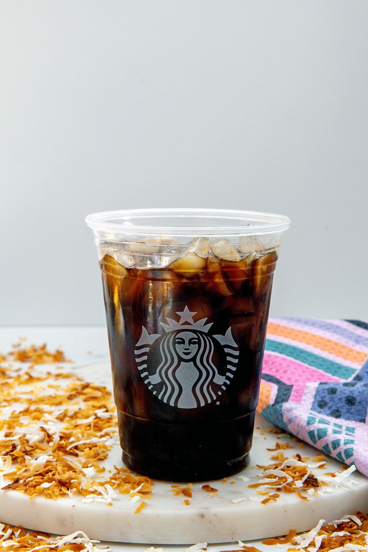 Head-on view of a Starbucks cup of cold brew with toasted shredded coconut all around.