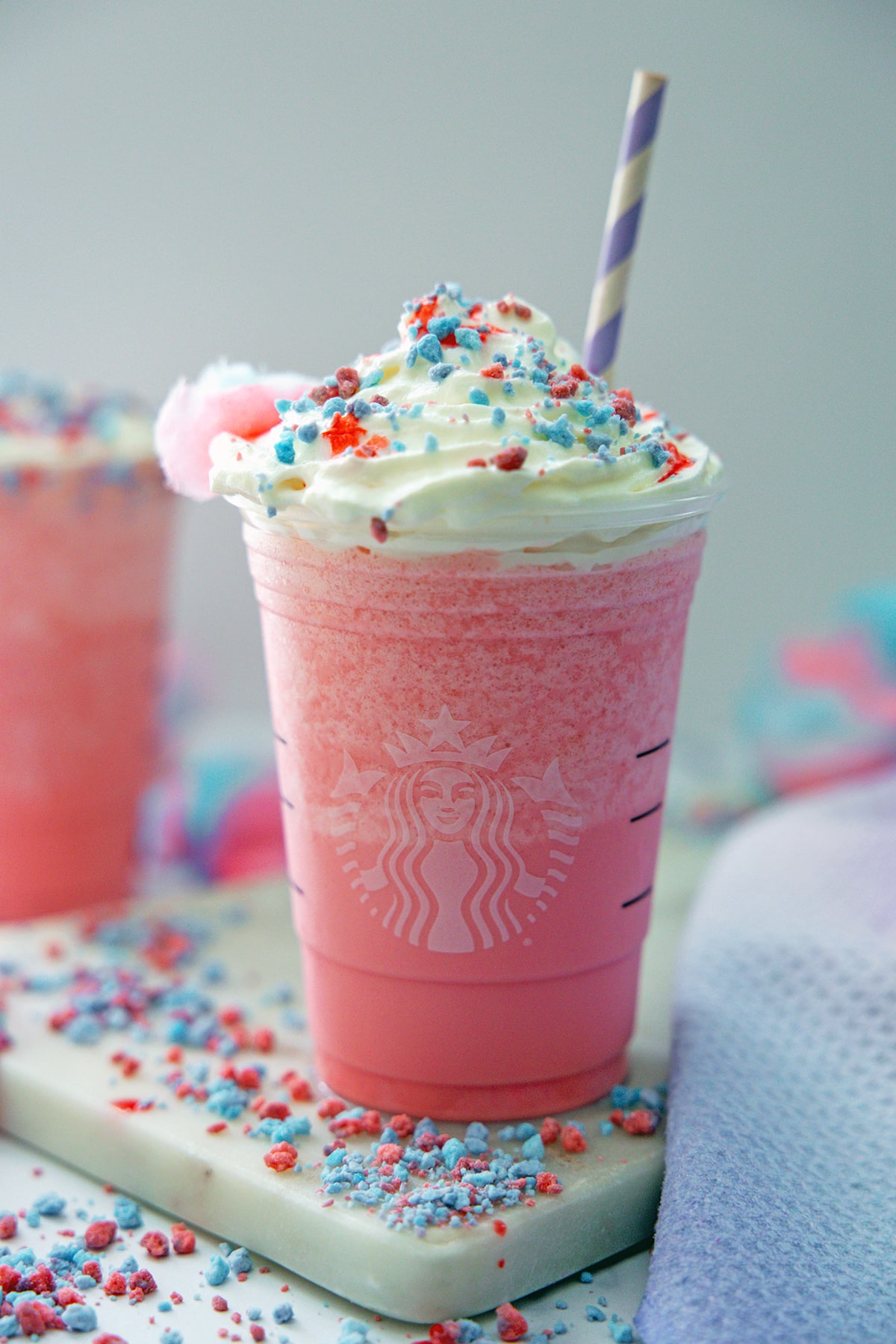 Head-on view of Cotton Candy Frappuccino i n a Starbucks cup with purple and white straw, whipped cream, and blue and pink sprinkles.