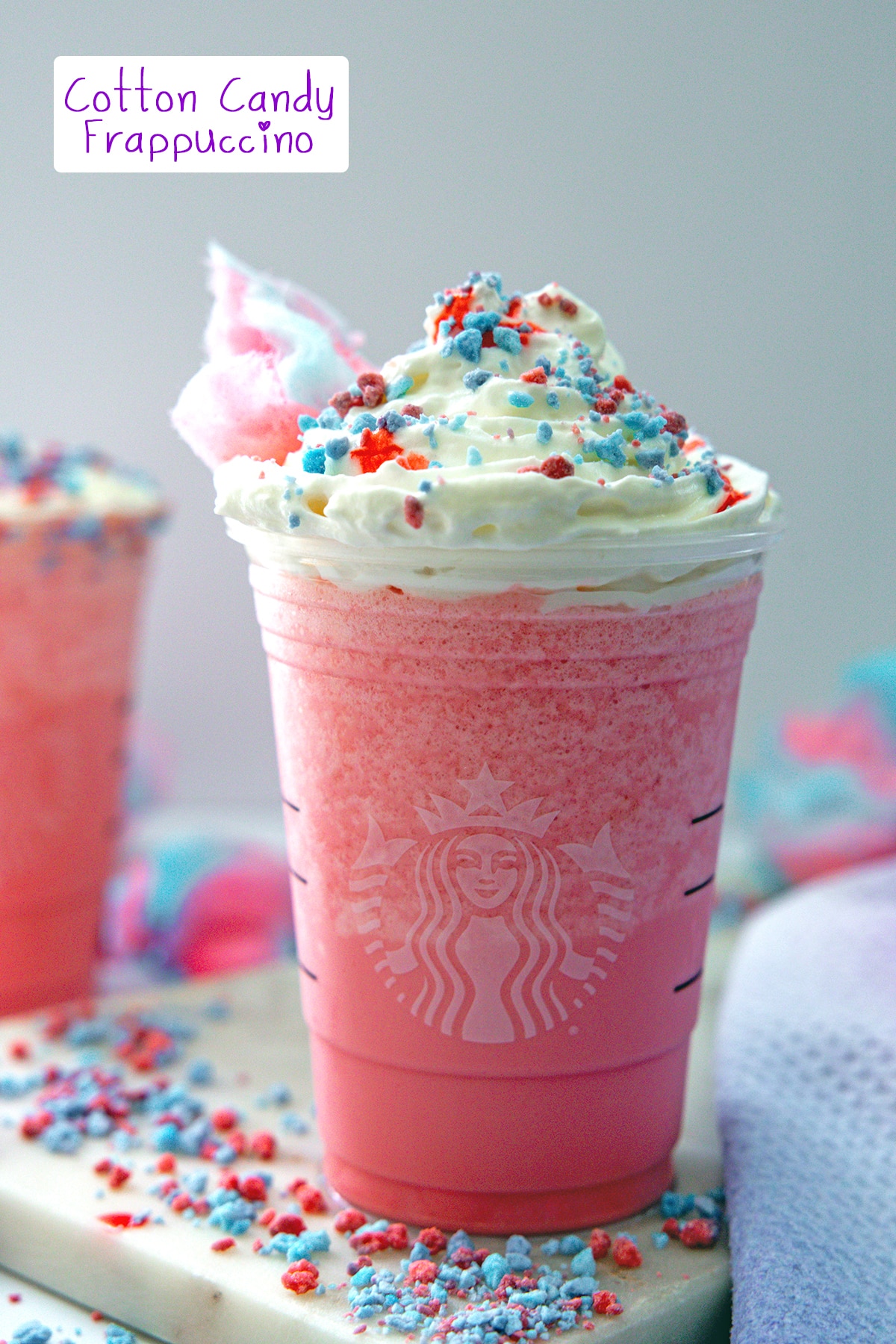 Head-on view of a pink Cotton Candy Frappuccino with pink and blue sprinkles and cotton candy all around.