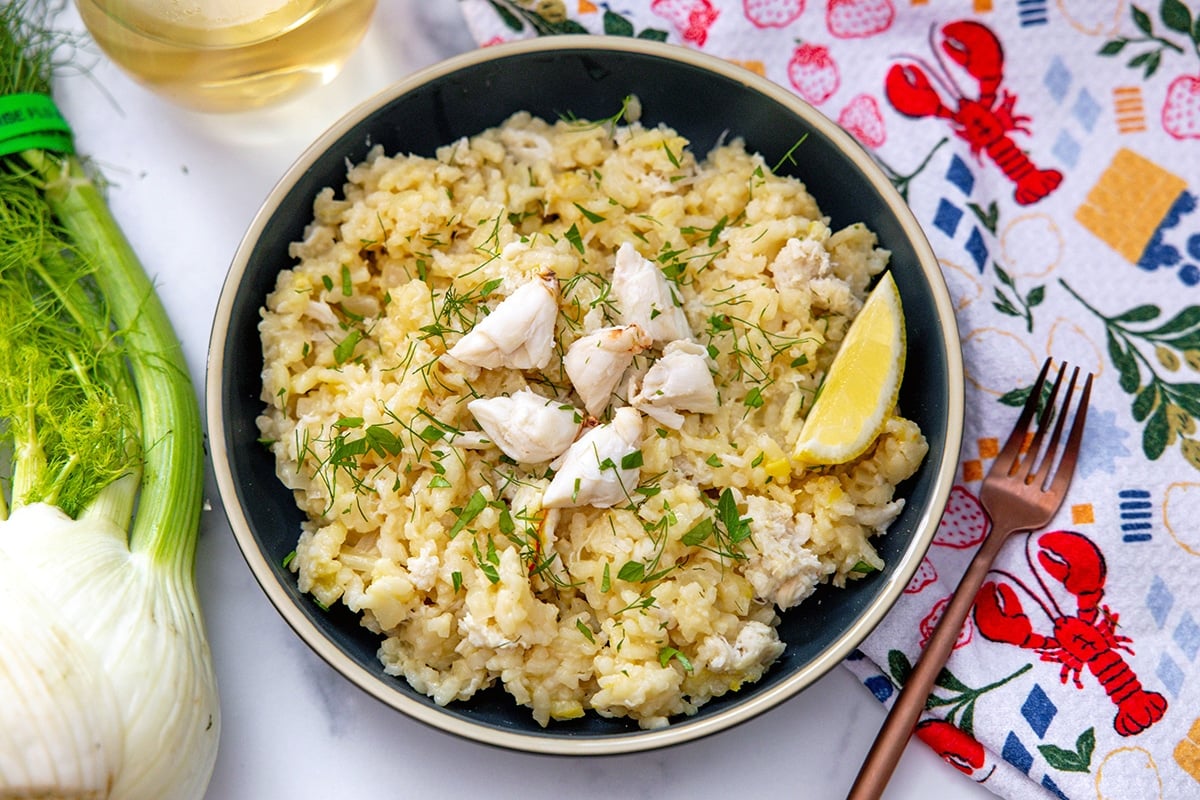Landscape overhead view of a bowl of crab risotto with fennel and glass of white wine on the side.