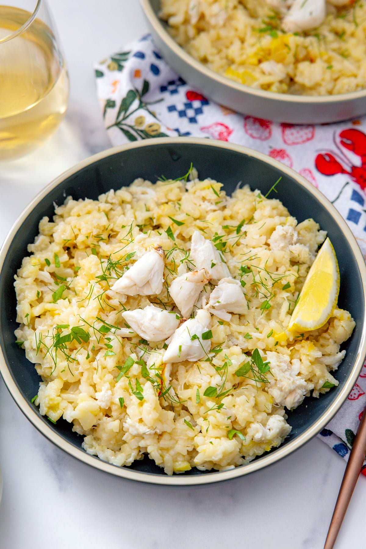Closeup view of a bowl of crab risotto with crab meat and lemon wedge on top.